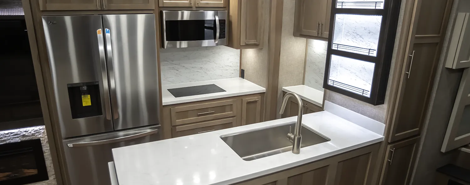 The Kitchen of a Luxe Elegante luxury fifth wheel with a modern design aesthetic and hardwood cabinetry.